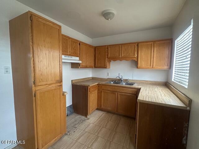 1137 Cimarron St, El Paso, TX 79915 - kitchen with under cabinet range hood, brown cabinetry, and light countertops
