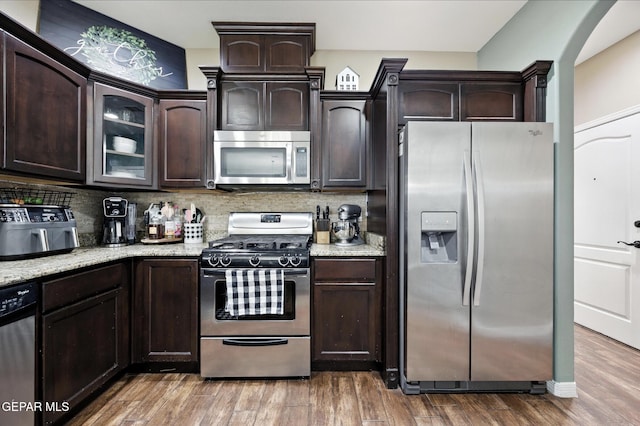 14516 Jesus Almeida, El Paso, TX 79938 - kitchen featuring appliances with stainless steel finishes, dark brown cabinetry, light stone counters, decorative backsplash, and glass insert cabinets