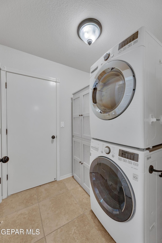 14304 Woods Point Ave, El Paso, TX 79938 - washroom featuring stacked washer / dryer, cabinet space, light tile patterned floors, and a textured ceiling