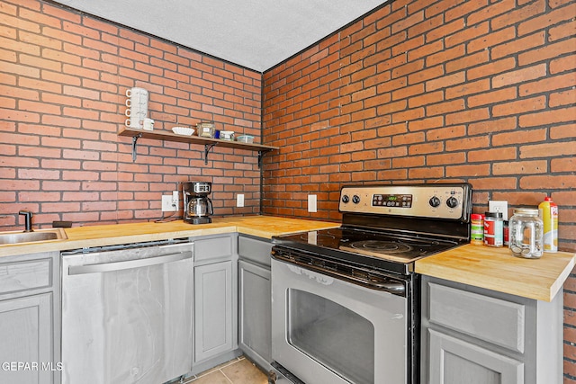 1624 Vinton Rd, Anthony, NM 88021 - kitchen featuring appliances with stainless steel finishes, butcher block counters, brick wall, open shelves, and light tile patterned floors