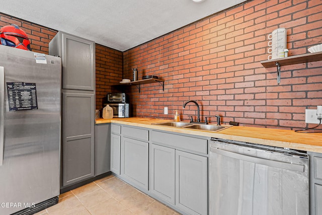 1624 Vinton Rd, Anthony, NM 88021 - kitchen featuring stainless steel appliances, open shelves, brick wall, gray cabinets, and wooden counters