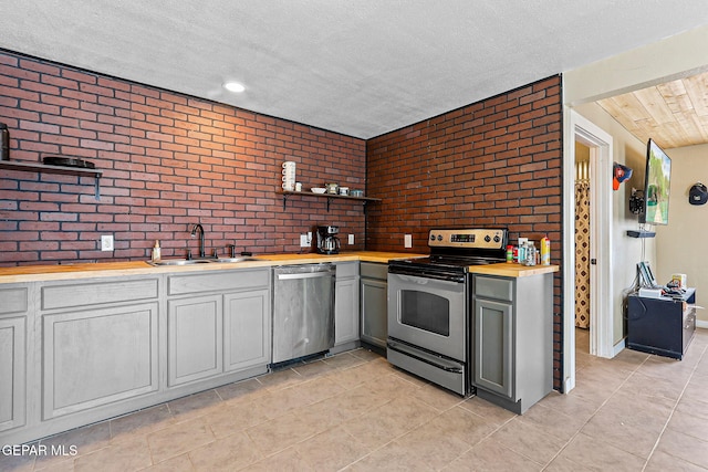 1624 Vinton Rd, Anthony, NM 88021 - kitchen featuring appliances with stainless steel finishes, wooden counters, open shelves, brick wall, and light tile patterned floors