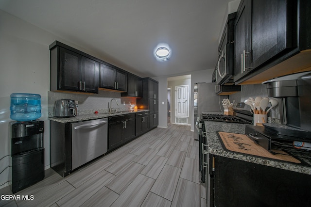 13163 Emerald Isle St, El Paso, TX 79928 - kitchen featuring stainless steel appliances, wood finish floors, light stone counters, dark cabinets, and decorative backsplash
