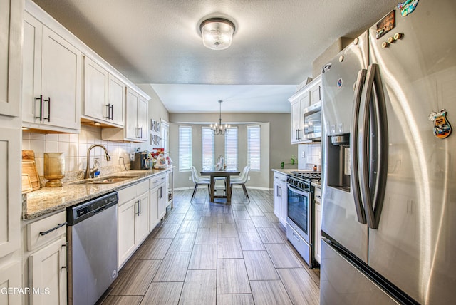 12140 Mesquite Thorn Dr, El Paso, TX 79934 - kitchen featuring stainless steel appliances, white cabinets, a chandelier, tasteful backsplash, and light stone countertops
