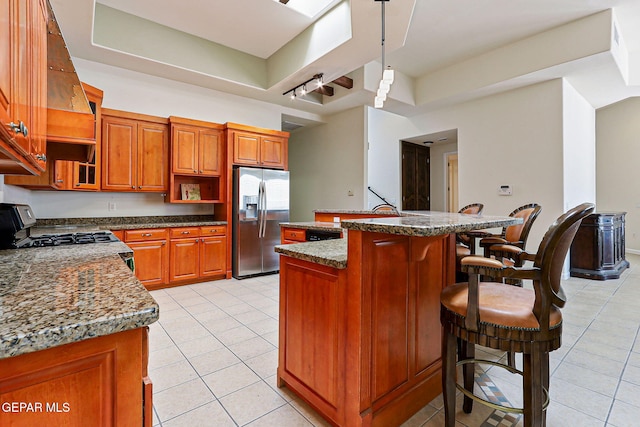 6514 Franklin Cove Place, El Paso, TX 79912 - kitchen featuring stainless steel refrigerator with ice dispenser, gas range, light tile patterned floors, a breakfast bar, and brown cabinetry