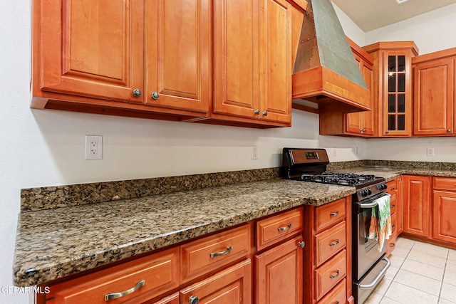 6514 Franklin Cove Place, El Paso, TX 79912 - kitchen with custom exhaust hood, stainless steel gas stove, light tile patterned floors, glass insert cabinets, and dark stone countertops