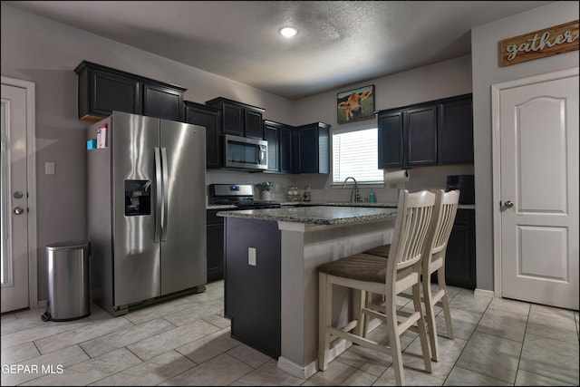 5949 Hidden Palms Dr, El Paso, TX 79924 - kitchen featuring stainless steel appliances, a breakfast bar area, a center island, dark cabinetry, and dark stone counters