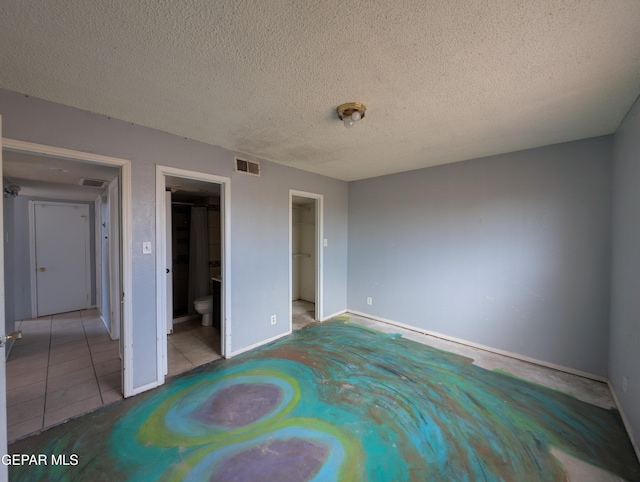 11828 Tracy Austin Ln, El Paso, TX 79936 - unfurnished bedroom featuring a textured ceiling, tile patterned flooring, a walk in closet, and ensuite bath