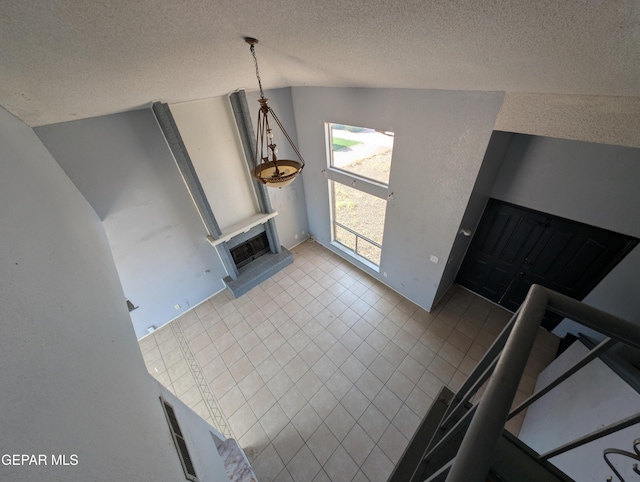 11828 Tracy Austin Ln, El Paso, TX 79936 - unfurnished living room featuring lofted ceiling, tile patterned flooring, a textured ceiling, and a fireplace with raised hearth