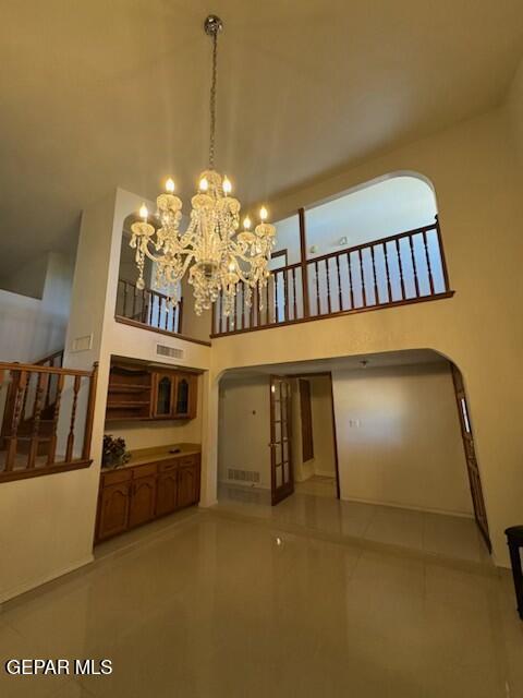 1718 Challenger Ln, El Paso, TX 79936 - unfurnished living room featuring a towering ceiling, tile patterned flooring, a chandelier, and arched walkways