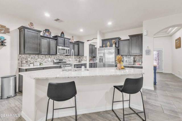 237 Gonzalo Cir, El Paso, TX 79932 - kitchen with arched walkways, stainless steel appliances, tasteful backsplash, a breakfast bar, and an island with sink