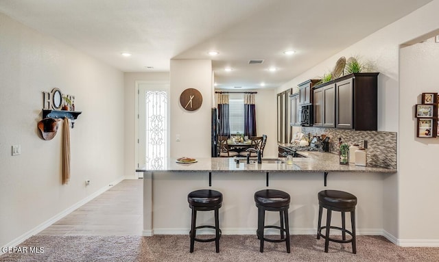 15249 Apex Ct, El Paso, TX 79938 - kitchen featuring black microwave, light stone counters, light colored carpet, a breakfast bar area, and a peninsula