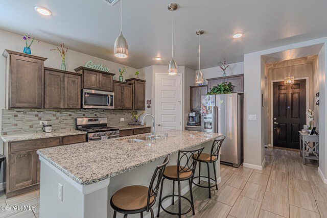 13010 Aberdare Dr, El Paso, TX 79928 - kitchen with stainless steel appliances, a breakfast bar, decorative backsplash, dark brown cabinetry, and decorative light fixtures