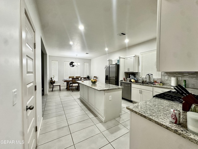 7780 Enchanted Park Dr, El Paso, TX 79911 - kitchen with stainless steel appliances, a kitchen island, light tile patterned floors, tasteful backsplash, and light stone counters