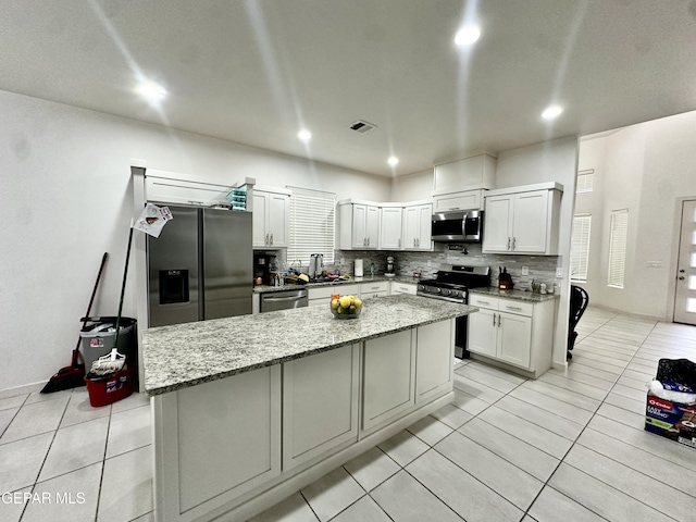 7780 Enchanted Park Dr, El Paso, TX 79911 - kitchen featuring stainless steel appliances, light tile patterned flooring, decorative backsplash, a center island, and light stone counters