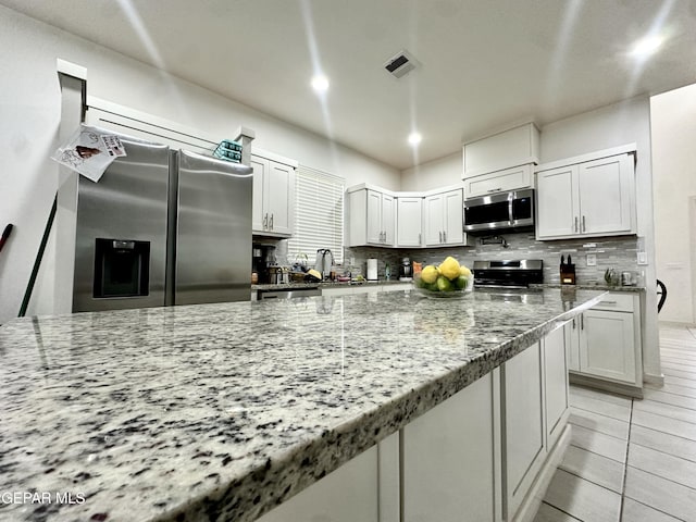 7780 Enchanted Park Dr, El Paso, TX 79911 - kitchen featuring stainless steel appliances, decorative backsplash, light stone counters, light tile patterned floors, and white cabinets