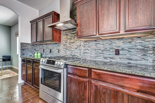 545 Lanner Dr, El Paso, TX 79928 - kitchen with stainless steel range with gas cooktop, wall chimney range hood, arched walkways, backsplash, and dark wood finished floors