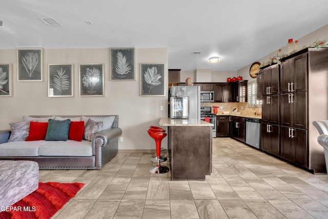 14192 Earl Chokiski, El Paso, TX 79938 - kitchen with stainless steel appliances, dark brown cabinetry, open floor plan, decorative backsplash, and a kitchen bar