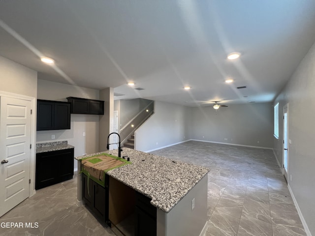 3720 Hill Top Place, El Paso, TX 79938 - kitchen with light stone countertops, a ceiling fan, a kitchen island with sink, and dark cabinets