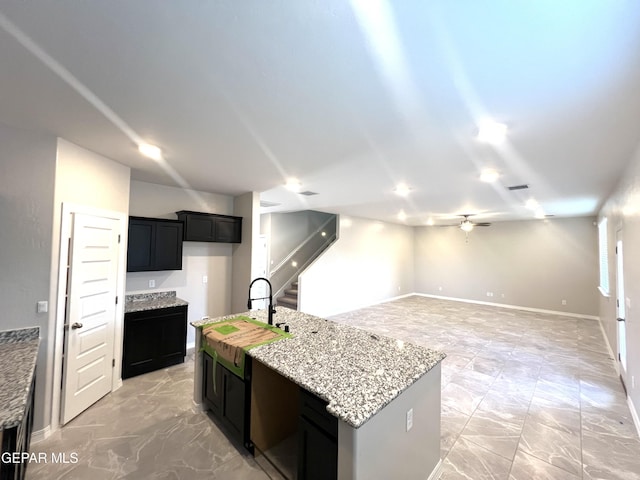 3720 Hill Top Place, El Paso, TX 79938 - kitchen with light stone countertops, ceiling fan, a center island with sink, and dark cabinets