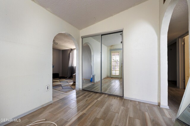123 Marquita Ln, El Paso, TX 79915 - unfurnished bedroom with arched walkways, wood finished floors, a closet, a textured ceiling, and lofted ceiling