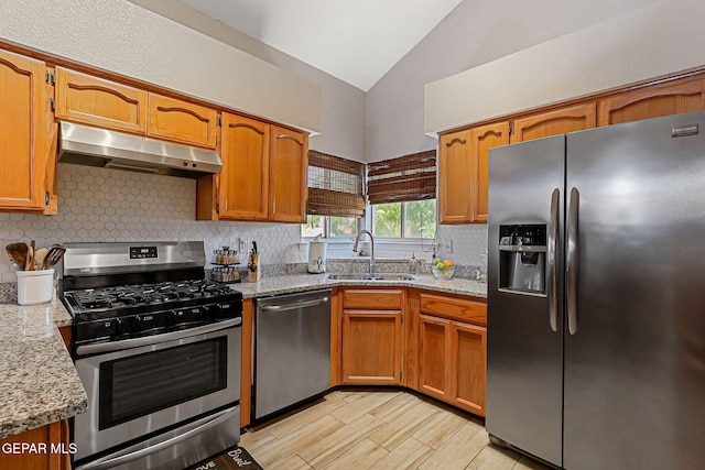700 Milton Henry Ave, El Paso, TX 79932 - kitchen featuring appliances with stainless steel finishes, under cabinet range hood, vaulted ceiling, tasteful backsplash, and brown cabinetry