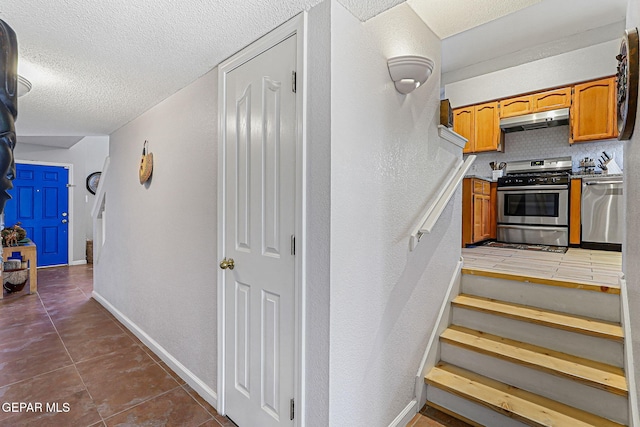 700 Milton Henry Ave, El Paso, TX 79932 - kitchen featuring stainless steel appliances, under cabinet range hood, a textured ceiling, brown cabinetry, and tile patterned floors