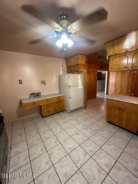 7190 Fatima Ave, El Paso, TX 79915 - kitchen featuring freestanding refrigerator, a ceiling fan, brown cabinetry, wooden walls, and light countertops