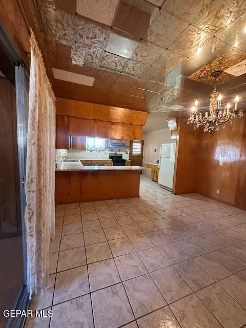 7190 Fatima Ave, El Paso, TX 79915 - kitchen with freestanding refrigerator, a chandelier, a peninsula, wooden walls, and stainless steel electric stove