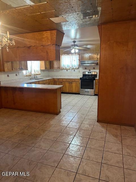 7190 Fatima Ave, El Paso, TX 79915 - kitchen featuring stainless steel range with gas cooktop, brown cabinetry, ceiling fan, a peninsula, and under cabinet range hood