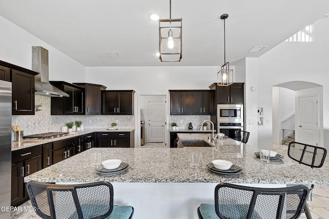 3725 Surmise St, El Paso, TX 79938 - kitchen featuring appliances with stainless steel finishes, wall chimney exhaust hood, arched walkways, tasteful backsplash, and a breakfast bar area
