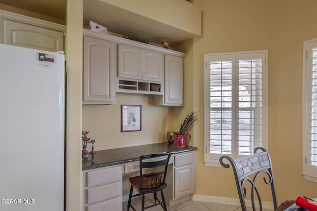 6316 Franklin Red Dr, El Paso, TX 79912 - kitchen with freestanding refrigerator, built in study area, light tile patterned floors, and dark stone counters