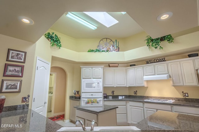 6316 Franklin Red Dr, El Paso, TX 79912 - kitchen featuring white appliances, white cabinets, a skylight, dark stone counters, and arched walkways