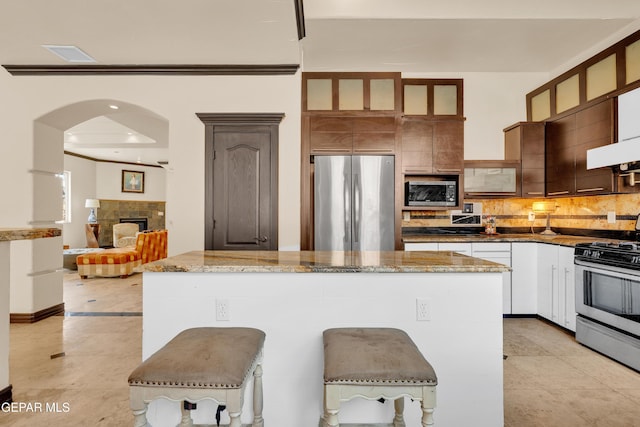4540 N Stanton St, El Paso, TX 79902 - kitchen featuring appliances with stainless steel finishes, backsplash, arched walkways, a kitchen island, and a breakfast bar area