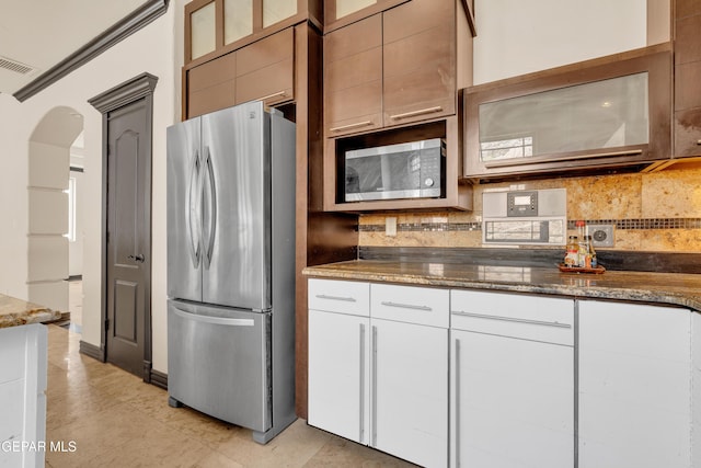 4540 N Stanton St, El Paso, TX 79902 - kitchen with freestanding refrigerator, arched walkways, backsplash, dark stone counters, and glass insert cabinets