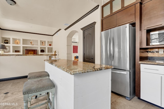4540 N Stanton St, El Paso, TX 79902 - kitchen with freestanding refrigerator, light stone counters, arched walkways, a center island, and glass insert cabinets