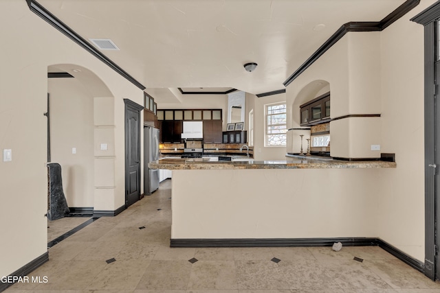 4540 N Stanton St, El Paso, TX 79902 - kitchen with freestanding refrigerator, a peninsula, arched walkways, stone countertops, and dark brown cabinets
