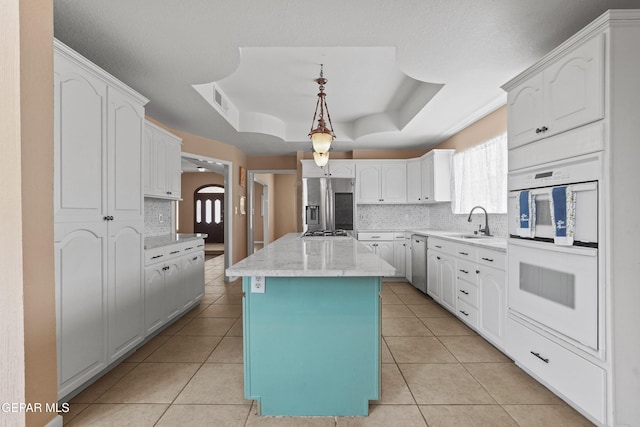 2072 Pueblo Nuevo Cir, El Paso, TX 79936 - kitchen with stainless steel appliances, a tray ceiling, light tile patterned floors, a kitchen island, and white cabinetry