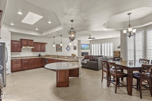 6688 Tuscany Ridge Dr, El Paso, TX 79912 - kitchen with a raised ceiling, a peninsula, appliances with stainless steel finishes, a kitchen breakfast bar, and a glass covered fireplace