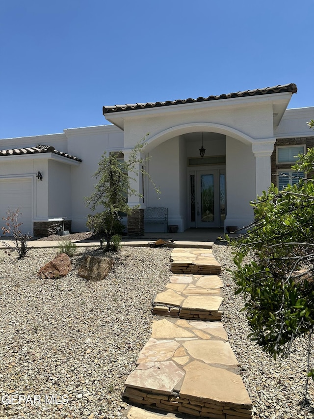 6688 Tuscany Ridge Dr, El Paso, TX 79912 - view of exterior entry featuring a tiled roof, an attached garage, stucco siding, and french doors