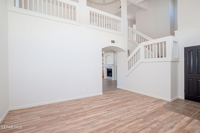 448 Ghost Flower St, Horizon City, TX 79928 - unfurnished living room featuring a high ceiling, wood finished floors, stairs, a fireplace, and arched walkways