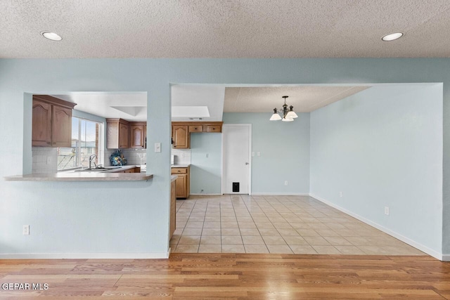 4821 Round Rock Dr, El Paso, TX 79924 - kitchen with a textured ceiling, a chandelier, light countertops, brown cabinets, and light wood-style floors
