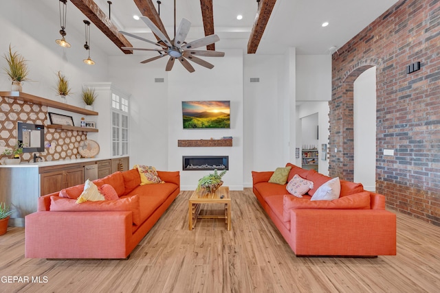 1042 Castillo Ct, El Paso, TX 79932 - living area featuring light wood finished floors, ceiling fan, a glass covered fireplace, brick wall, and beamed ceiling