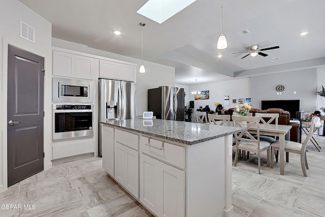 2362 Enchanted Crown Ln, El Paso, TX 79911 - kitchen featuring stainless steel appliances, a skylight, a kitchen island, dark stone counters, and white cabinetry