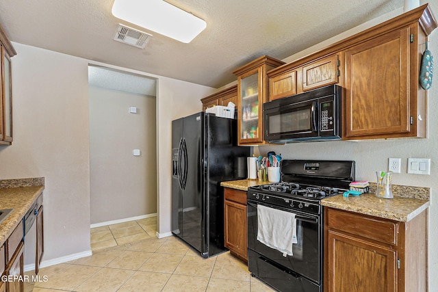 13344 Jonathan Elias Ct, El Paso, TX 79938 - kitchen with black appliances, light tile patterned floors, glass insert cabinets, brown cabinets, and a textured ceiling