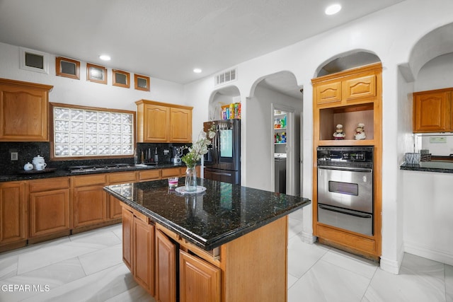 12247 Chisholm Pass Dr, El Paso, TX 79936 - kitchen featuring stainless steel appliances, a warming drawer, arched walkways, decorative backsplash, and dark stone counters