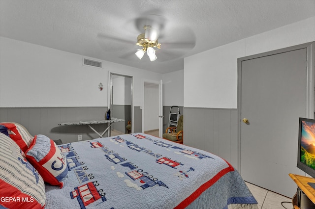 11749 Socorro Rd, Socorro, TX 79927 - bedroom featuring a wainscoted wall, a textured ceiling, a ceiling fan, and light tile patterned floors
