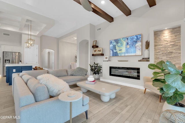 7424 Cimarron Gap Dr, El Paso, TX 79911 - living room featuring beamed ceiling, arched walkways, light wood-style floors, a glass covered fireplace, and a chandelier