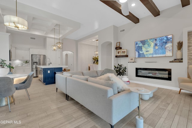 7424 Cimarron Gap Dr, El Paso, TX 79911 - living room featuring beamed ceiling, light wood-style floors, ceiling fan, a glass covered fireplace, and arched walkways