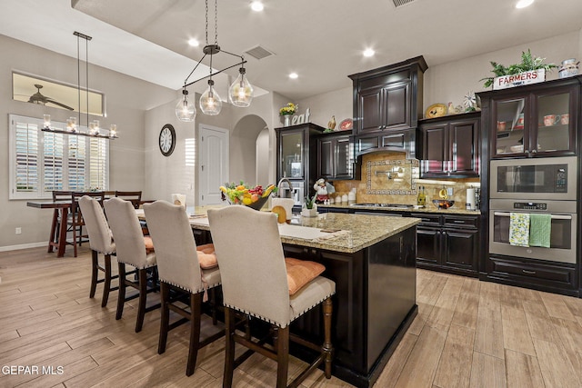 12289 Freshwater Dr, El Paso, TX 79928 - kitchen featuring stainless steel appliances, arched walkways, light wood-type flooring, tasteful backsplash, and an island with sink